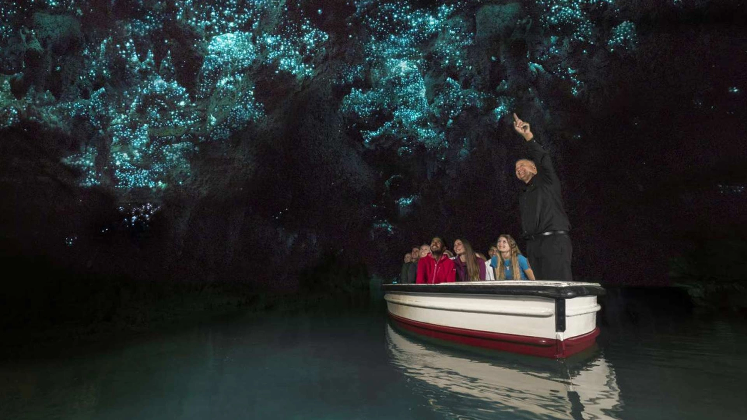 Group of people take a boat tour through glow worm caves