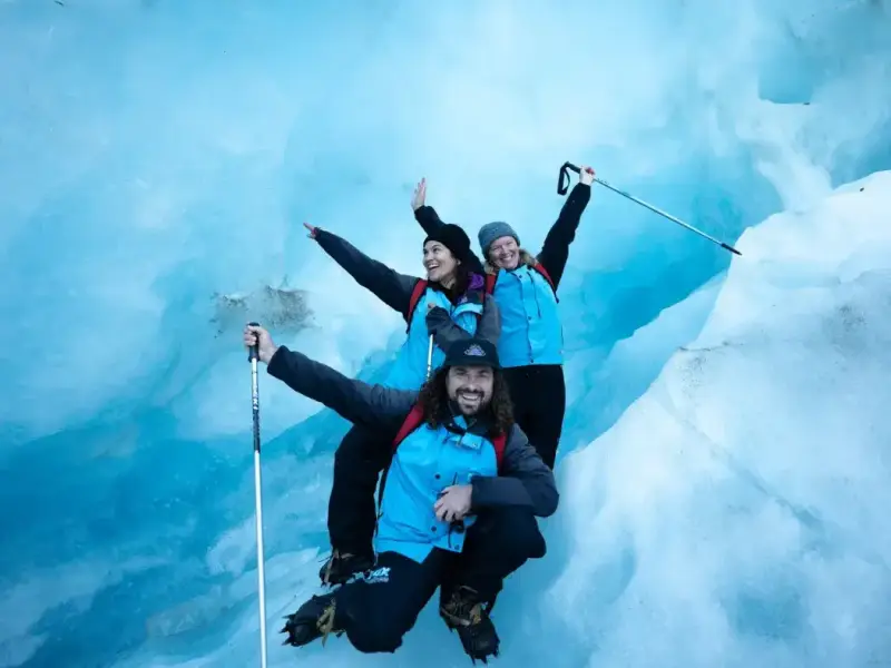 Travellers exploring a bright blue ice cave on Franz Josef Glacier, highlighting one of the best winter adventure activities in New Zealand with glacier hiking, icy landscapes and South Island scenery beyond the ski fields.