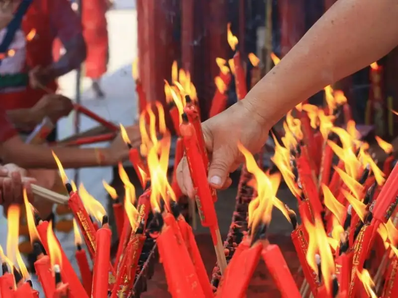 Hands lighting red candles and incense at a temple during Lunar New Year, reflecting Chinese New Year customs of prayer, gratitude, honouring ancestors, and welcoming good fortune for the year ahead.