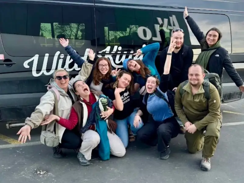 Group photo of youth backpackers throwing hands in the air and happy after a Wild Kiwi tour across New Zealand.