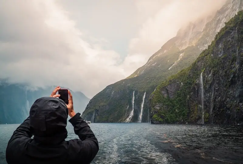 Photo of a person taking a photo of waterfalls in Milford Sound New Zealand.