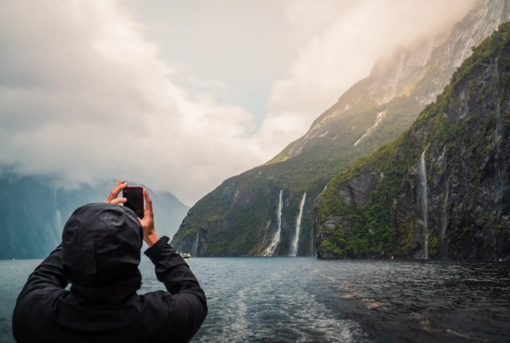 Photo of a person taking a photo of waterfalls in Milford Sound New Zealand.