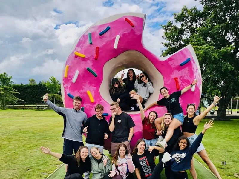 Group of travellers posing around a giant pink donut sculpture at a quirky roadside attraction in New Zealand.