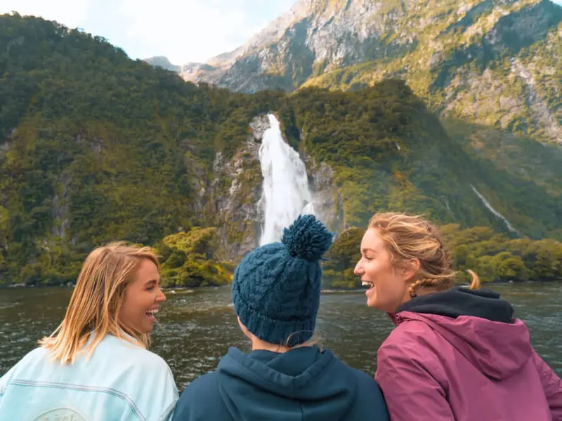 A group of female travellers on a Milford Sound cruise in Autumn laugh and enjoy the weather while visiting on their Wild Kiwi small group tour of the South Island.
