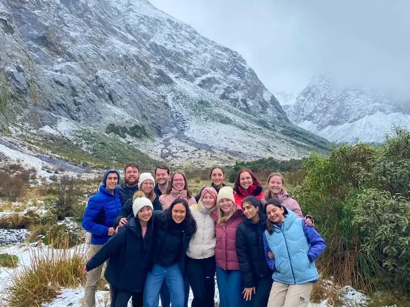 Group of travellers posing in front of snow-capped mountains during a New Zealand South Island winter tour hike in Fiordland National Park