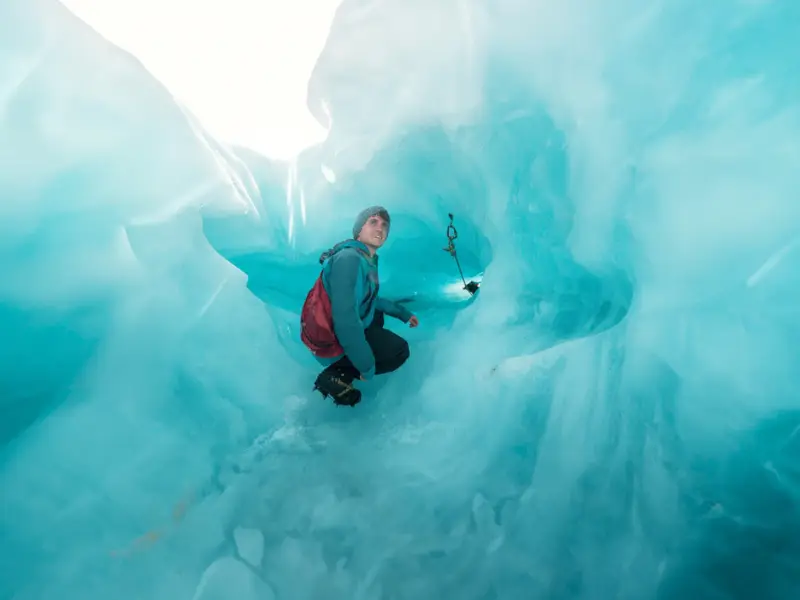 A young male traveller sits in an ice cave on Franz Josef Glacier on a New Zealand small group tour of the South Island during a helicopter-hike glacier tour.