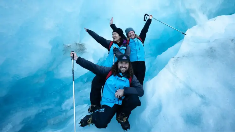 Group of hikers celebrating on a guided glacier hike in Franz Josef, New Zealand during winter adventure tour.