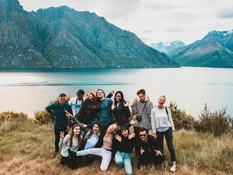 A group of young adventure travellers making goofy faces and laughing while posing in front of snowy mountains near queenstown, while on a winter New Zealand tour.