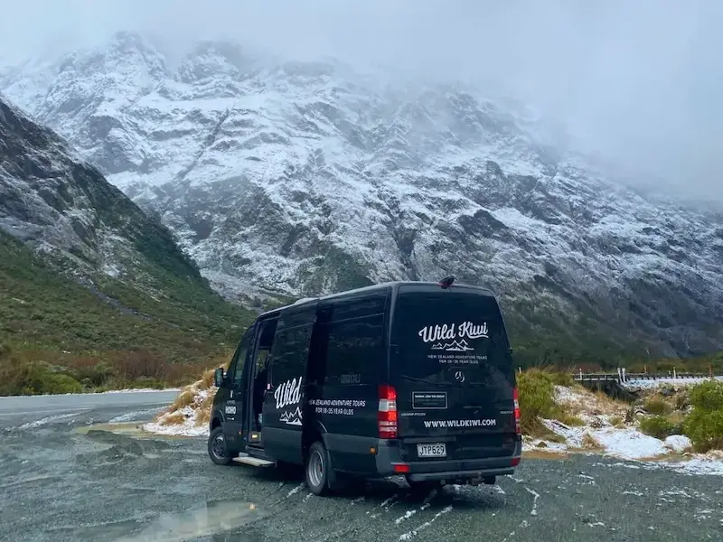 Wild Kiwi tour van driving through snow-dusted alpine road in New Zealand’s South Island during winter adventure tour.