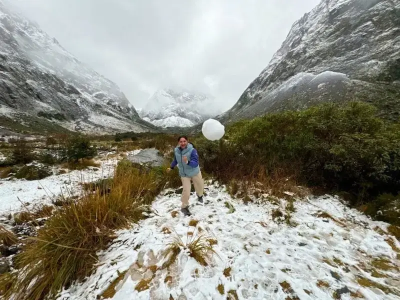 Solo female traveller throwing a snowball with a snow-covered mountain backdrop while on a winter New Zealand tour with Wild Kiwi.