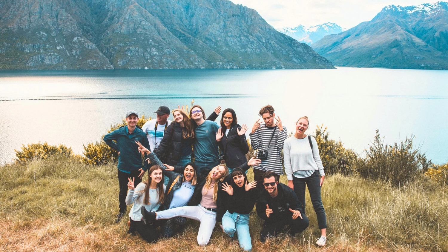 A group of young adventurous travellers posing before Queenstown and lakes while exploring New Zealand in Autumn on a small group tour with Wild Kiwi.