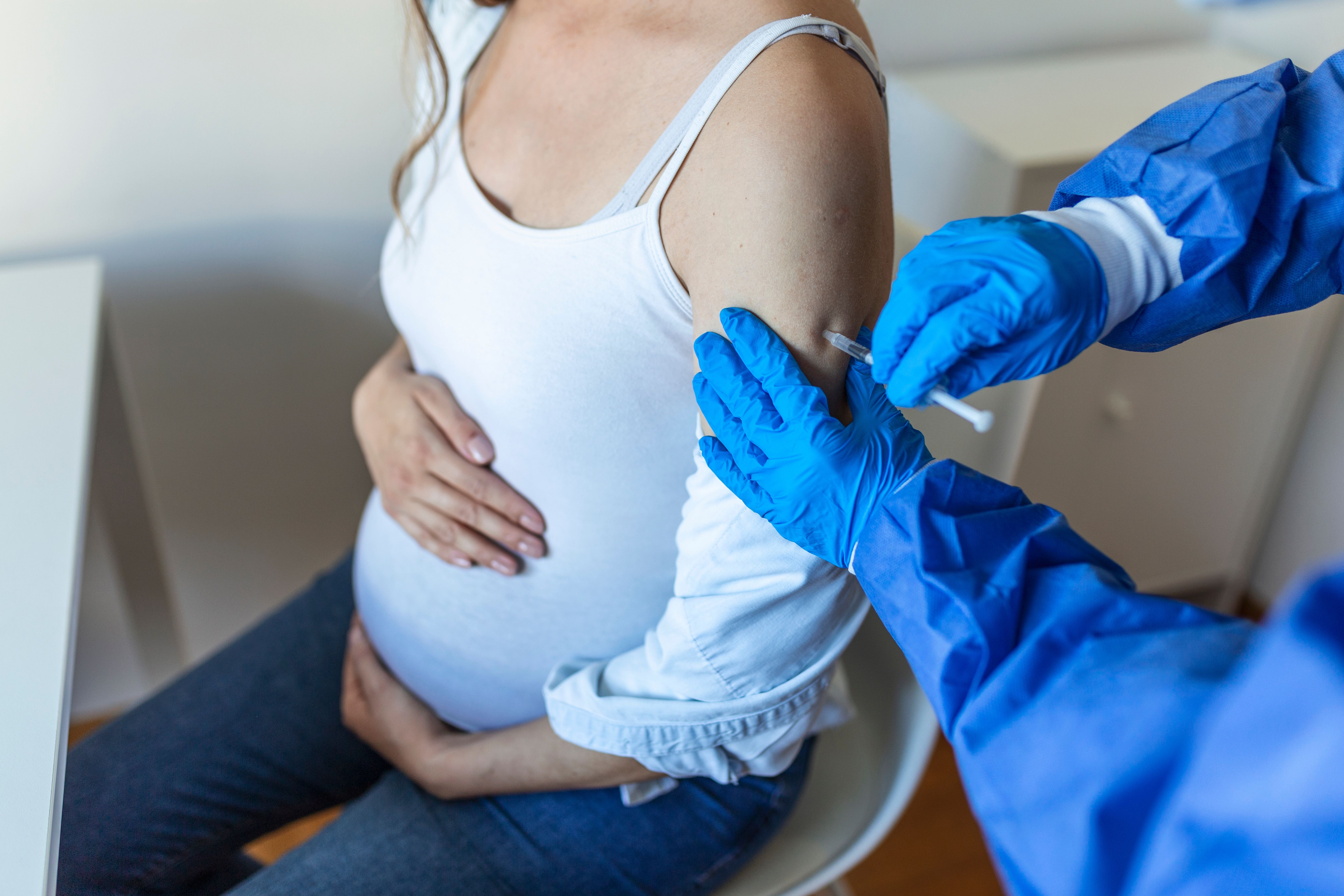 A pregnant woman receives a vaccination in her upper arm from a gloved clinician.