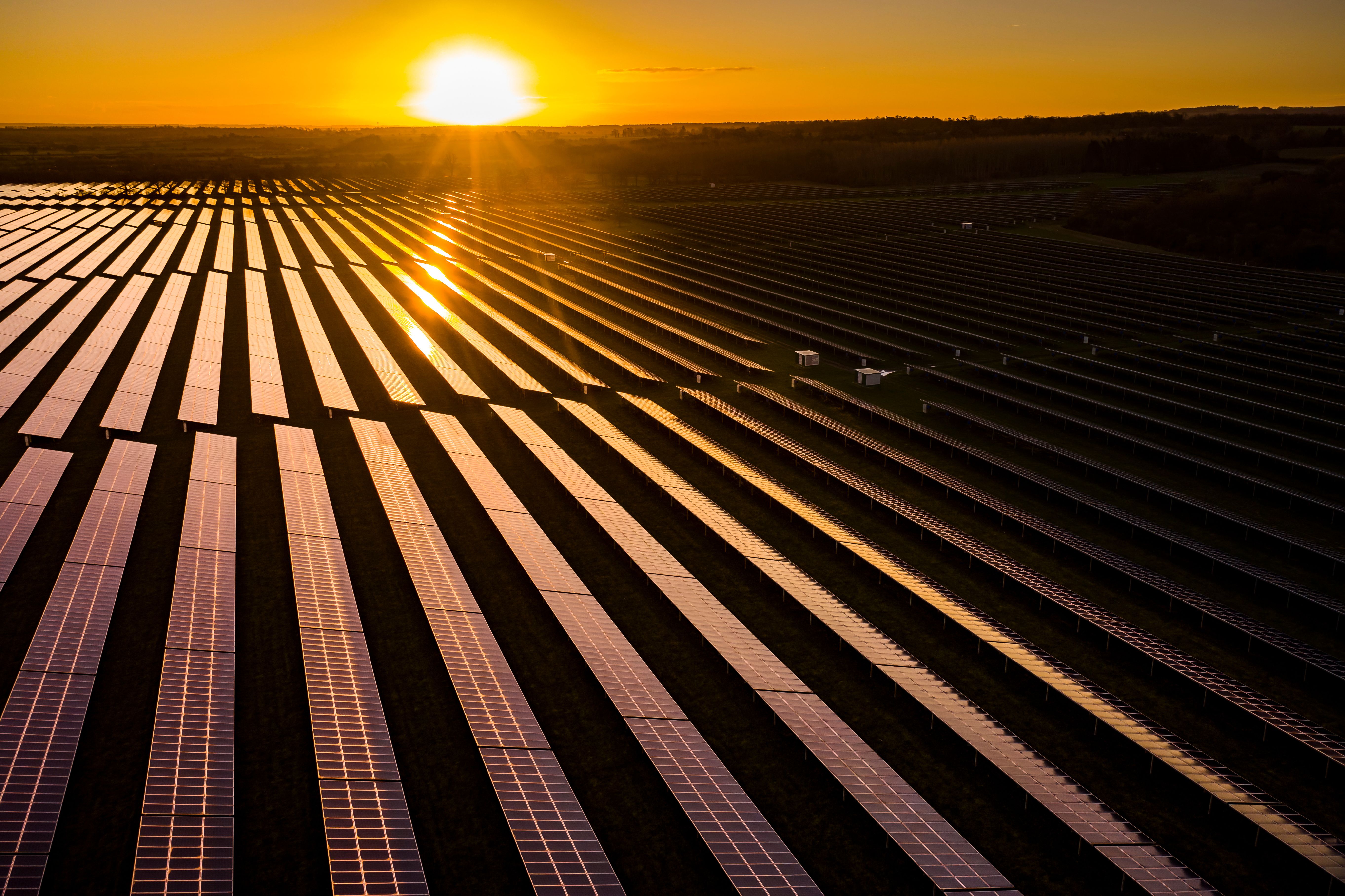 Aerial view of a large solar farm at sunrise, rows of photovoltaic panels stretching across the English countryside