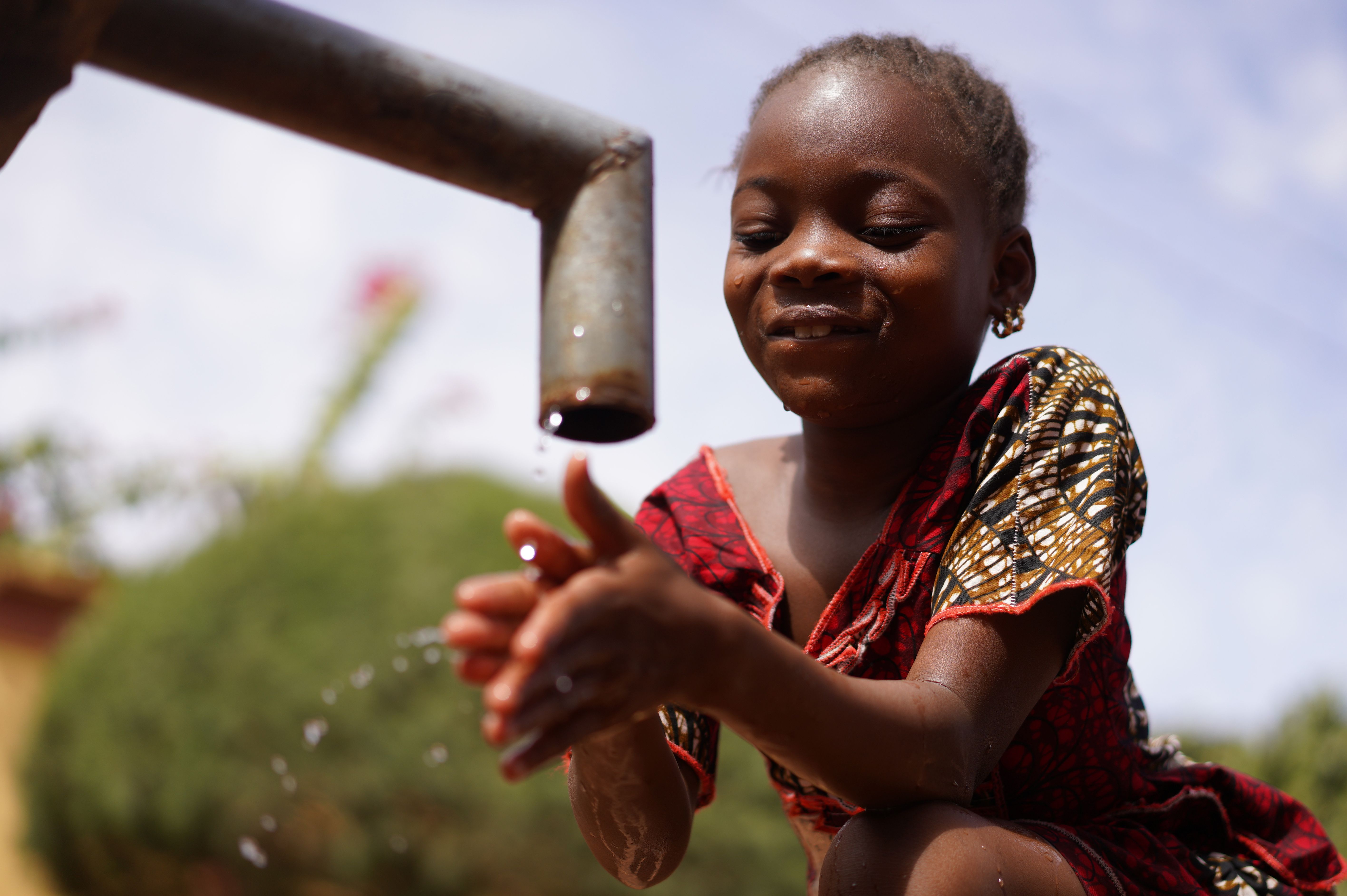 A young girl smiles as she washes her hands under clean running water from an outdoor tap