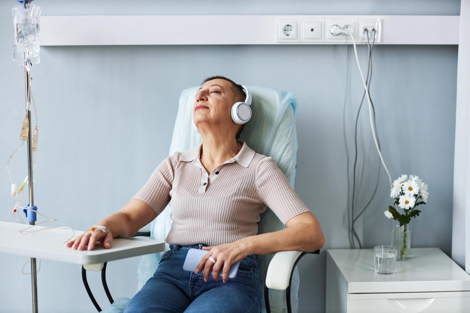 A woman relaxes with headphones while receiving an intravenous drip during treatment in a hospital infusion chair