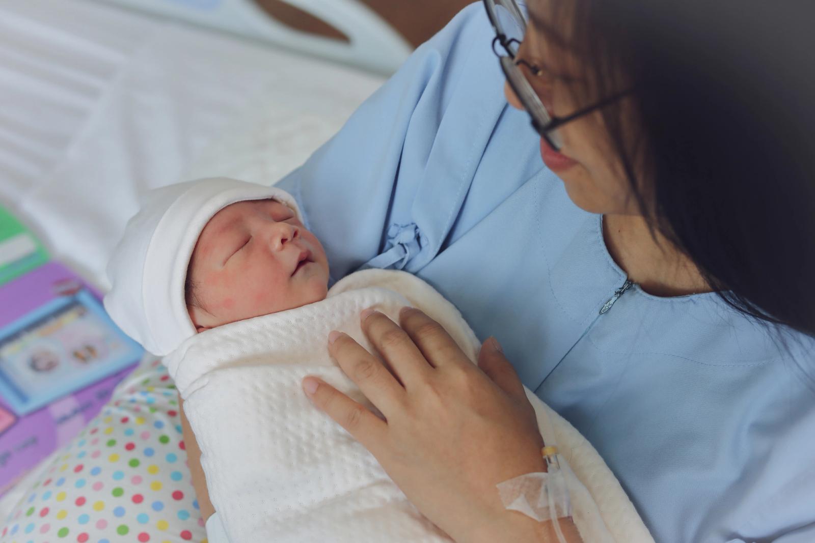 A mother rests in a hospital bed after childbirth, holding her newborn