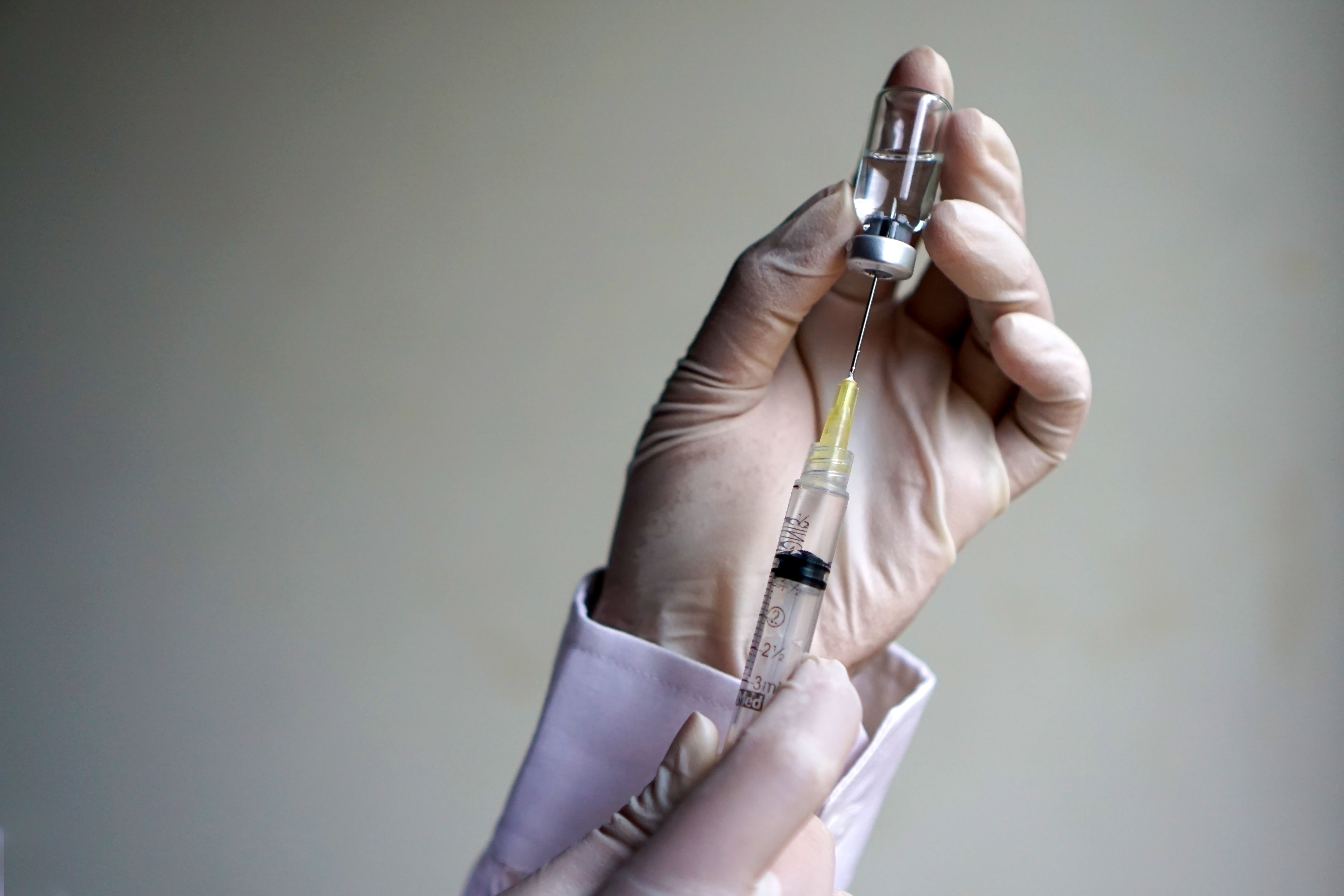 A gloved hand holding a medicine vial and a syringe