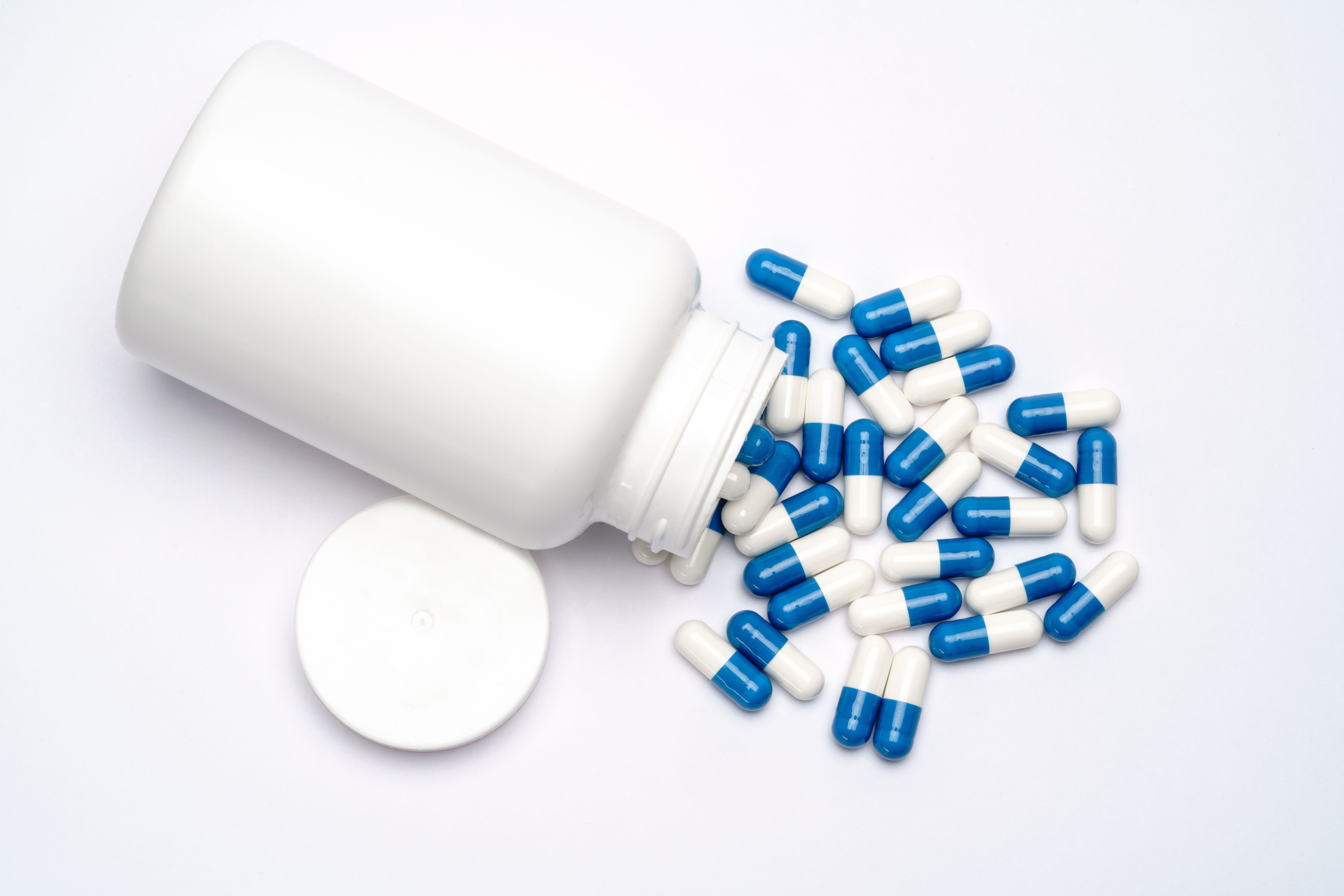Prescription medicine capsules beside a plain white pill bottle on a grey surface