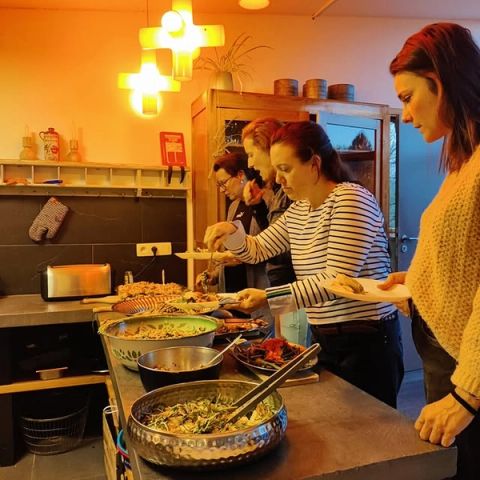 Deelnemers scheppen eten op aan een buffet met verse salades en gerechten in een gezellige keuken