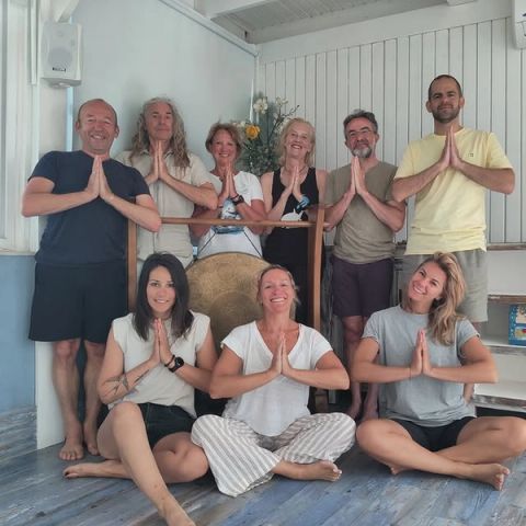 Groep deelnemers en begeleiders glimlachend met de handen in gebedshouding in de yogaruimte