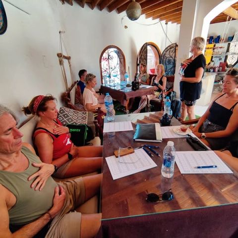 Groep deelnemers rond een tafel met gesloten ogen en handen op de borst tijdens een ademsessie