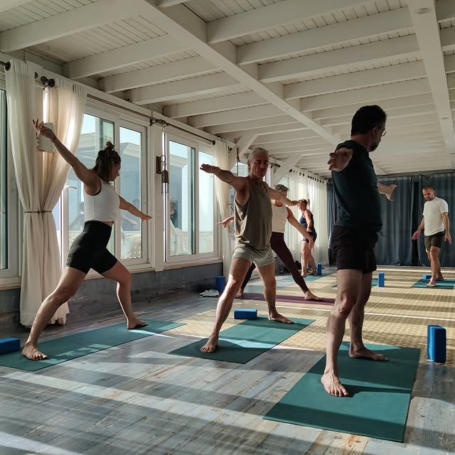 Mensen in krijgerhouding op yogamatten in een lichte yogaruimte met houten balken