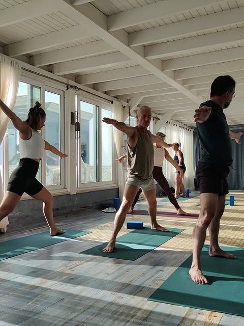 Mensen in krijgerhouding op yogamatten in een lichte yogaruimte met houten balken