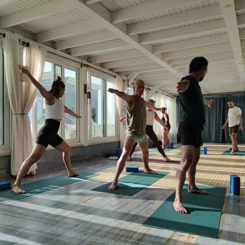 Mensen in krijgerhouding op yogamatten in een lichte yogaruimte met houten balken