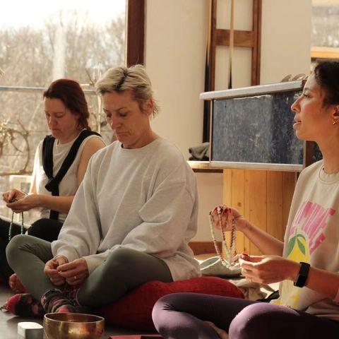 Drie vrouwen zittend op de vloer tijdens een meditatiesessie met malakettingen en een klankschaal