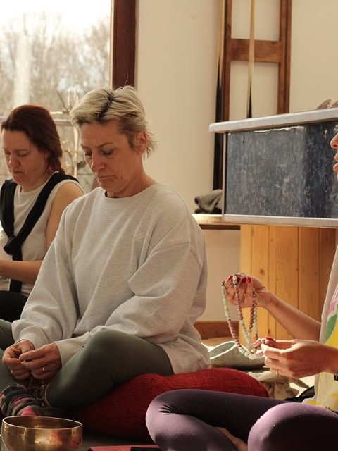 Drie vrouwen zittend op de vloer tijdens een meditatiesessie met malakettingen en een klankschaal
