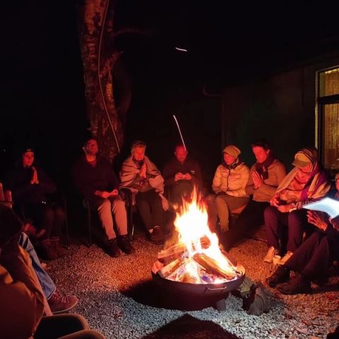 Deelnemers van een retreat zitten 's avonds in een kring rond een brandende vuurschaal in de Eifel