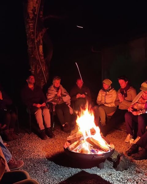 Deelnemers van een retreat zitten 's avonds in een kring rond een brandende vuurschaal in de Eifel