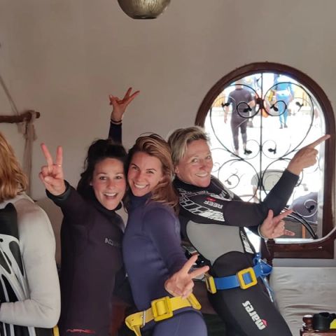 Drie lachende vrouwen in wetsuit en loodgordel poseren vrolijk voor hun duiksessie in Dahab