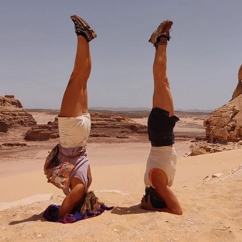 Two people practising headstands in the sand with rock formations and desert landscape in the Sinai behind them