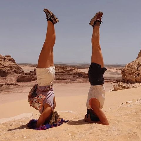Two people practising headstands in the sand with rock formations and desert landscape in the Sinai behind them