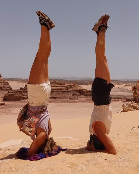 Two people practising headstands in the sand with rock formations and desert landscape in the Sinai behind them