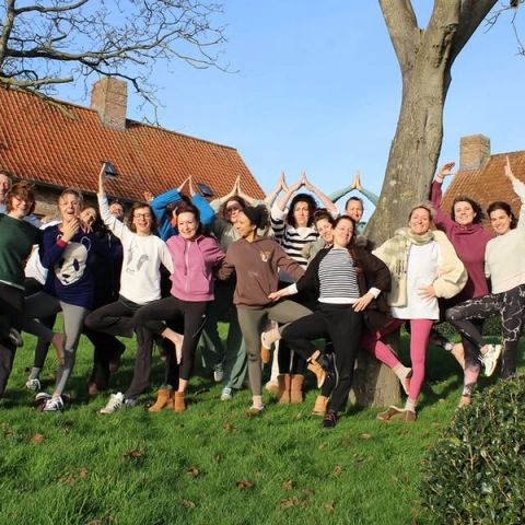 Een groep deelnemers lacht en balanceert samen in de boomhouding op het gras in de tuin