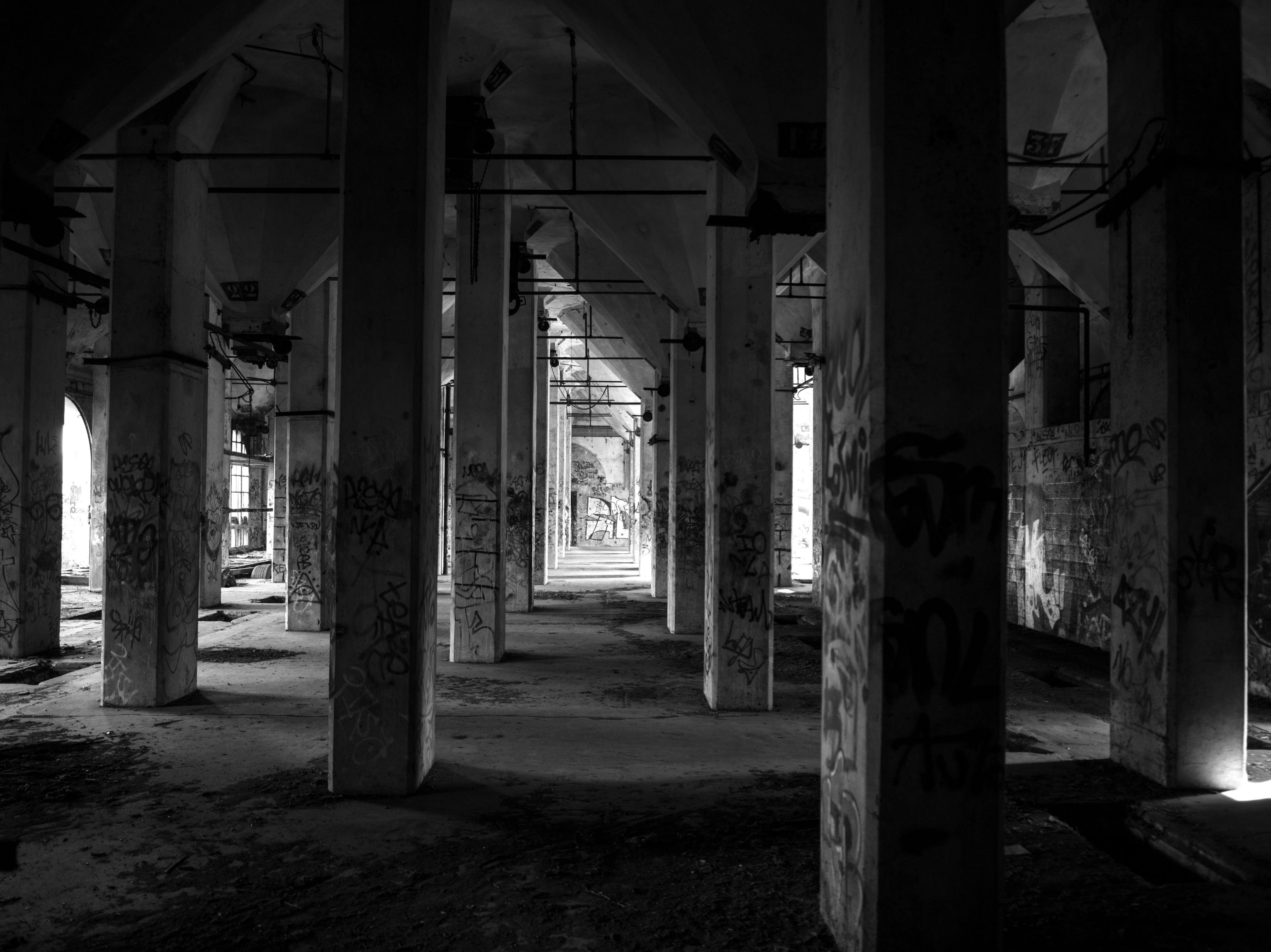 Black and white urbex photograph of concrete pillars beneath the former mill in Marquette-lez-Lille, with graffiti, abandoned industrial architecture and strong shadow contrasts.