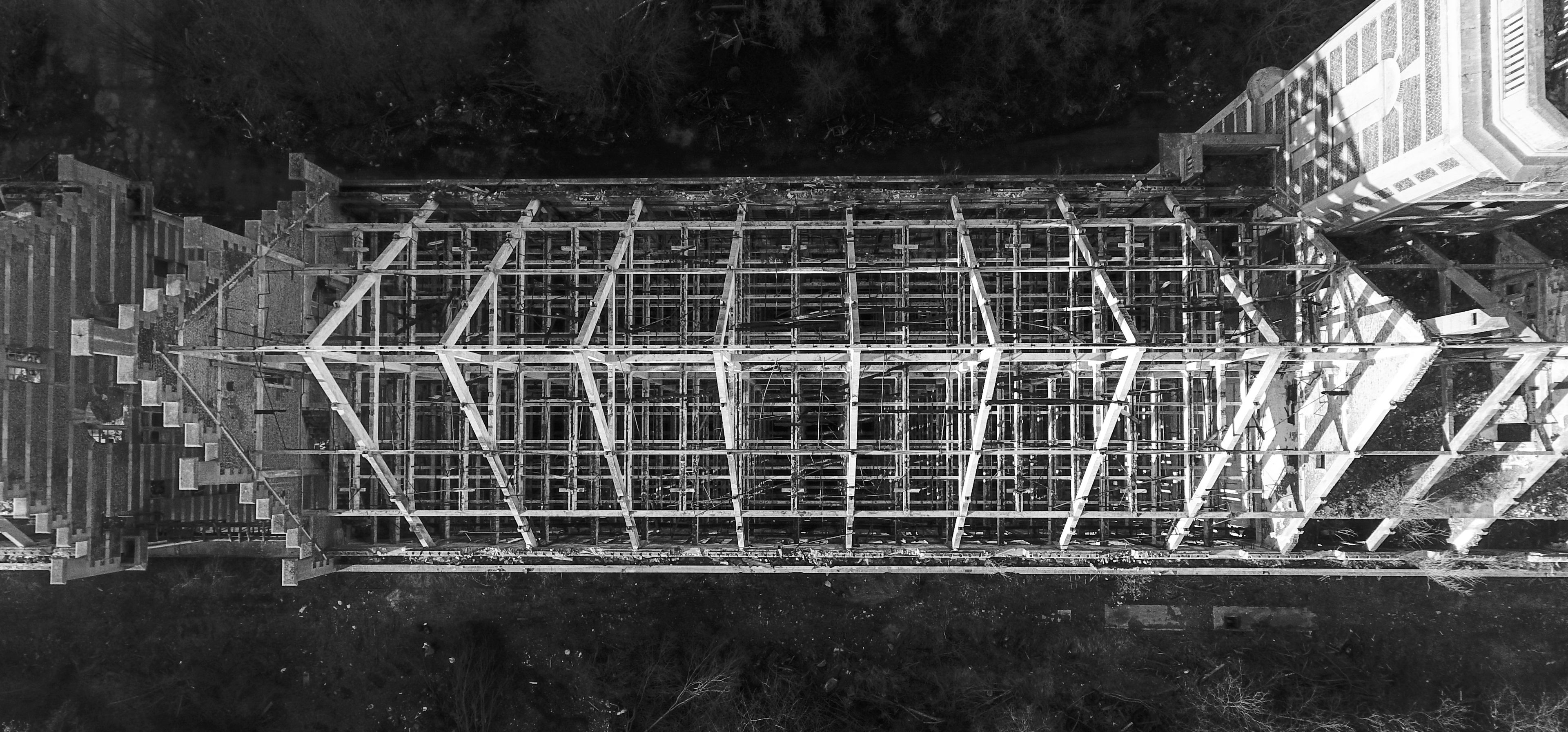 Black and white overhead urbex photograph of the abandoned former mill in Marquette-lez-Lille, showing the roofless industrial structure, exposed beams and geometric concrete framework.