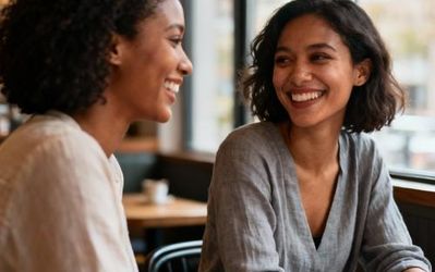 Two women from different cultural backgrounds having coffee and smiling at each other in a cozy café