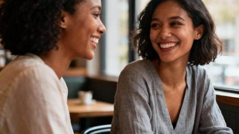 Two women from different cultural backgrounds having coffee and smiling at each other in a cozy café