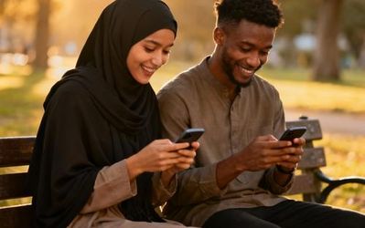 Young Muslim couple sitting together in a peaceful garden setting, both looking at their smartphones with gentle smiles