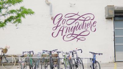 Chase brand film woman walking bicycle in front of wall with painted text Go Anywhere