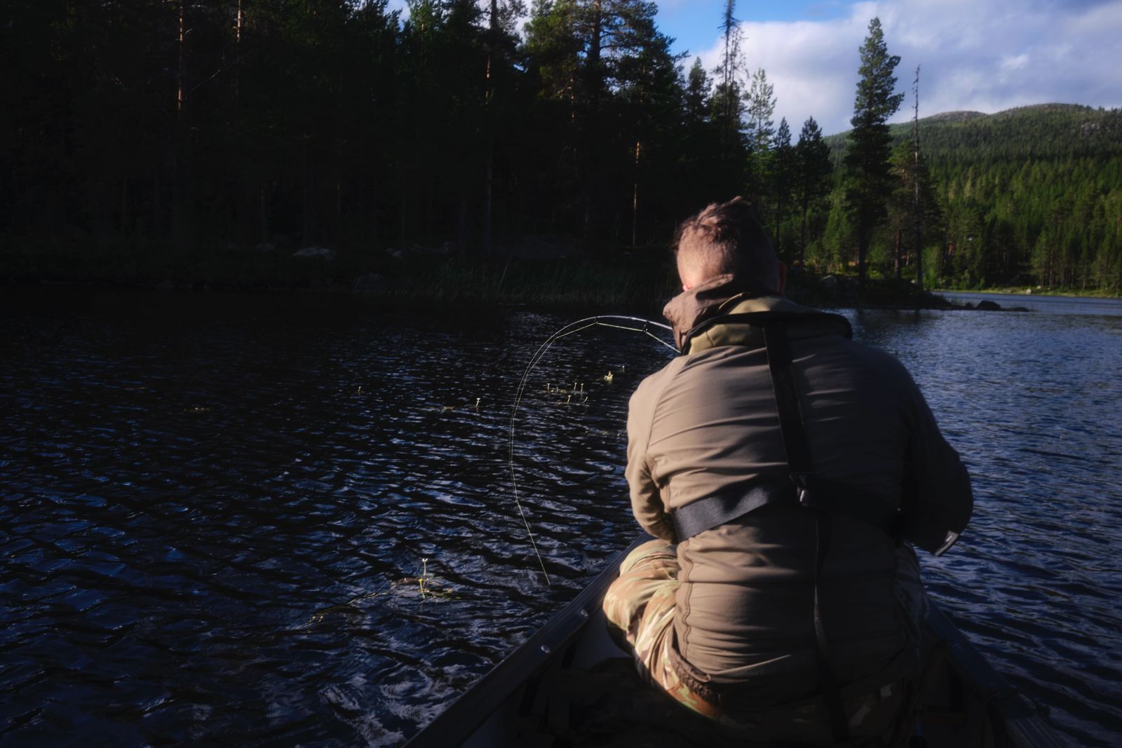 Mann im Kanu beim Angeln auf einem ruhigen See in Schweden, Rückansicht.