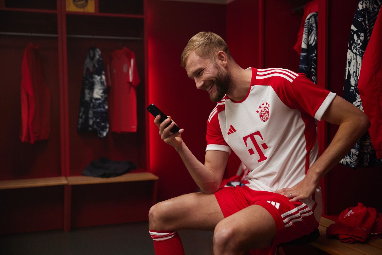 Konrad Laimer sitzt lächelnd mit seinem Smartphone in den Kabinen der Allianz Arena für die Bitpanda-Werbekampagne, fotografiert von Karl Scholten.