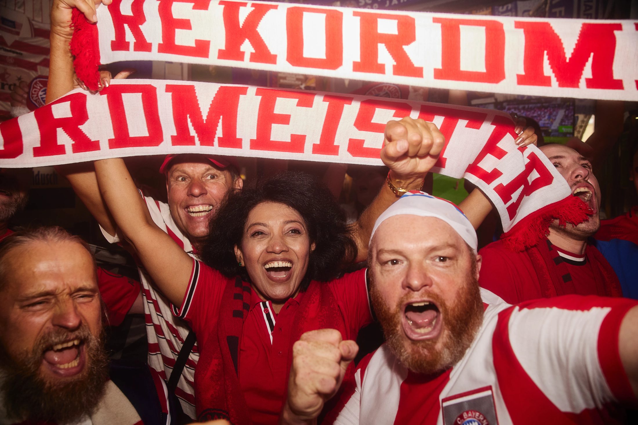 Fußballfans feiern ausgelassen in einer urigen Fankneipe mit ‚Rekordmeister‘-Schal