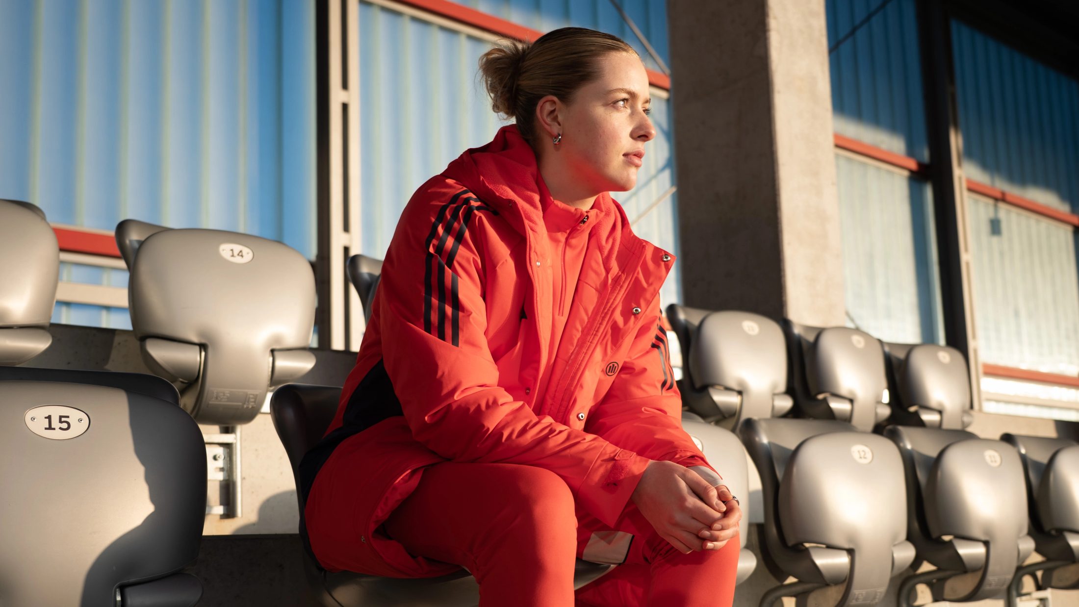 Porträtaufnahme von FC Bayern Spielerin Alara Şehitler in roter Team-Kleidung, die nachdenklich auf der Stadiontribüne sitzt; fotografiert von Karl Scholten.