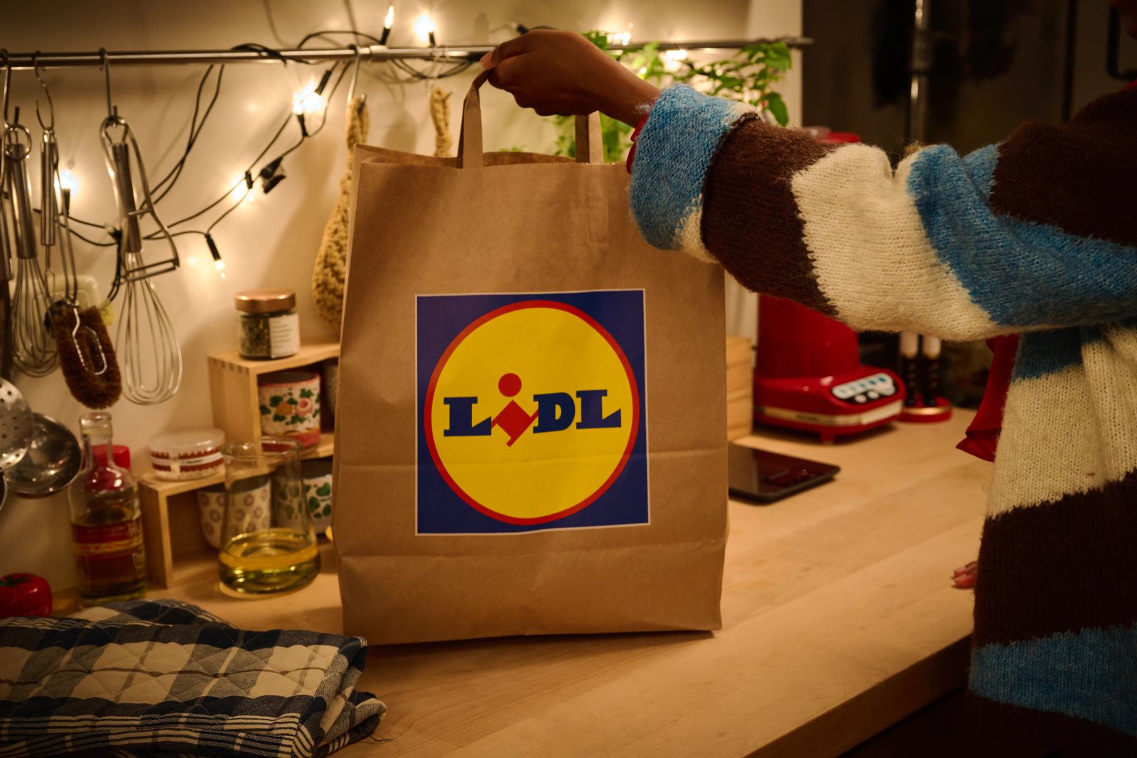 Eine Person hält eine Lidl-Papiertüte in einer weihnachtlich dekorierten Küche am Griff hoch