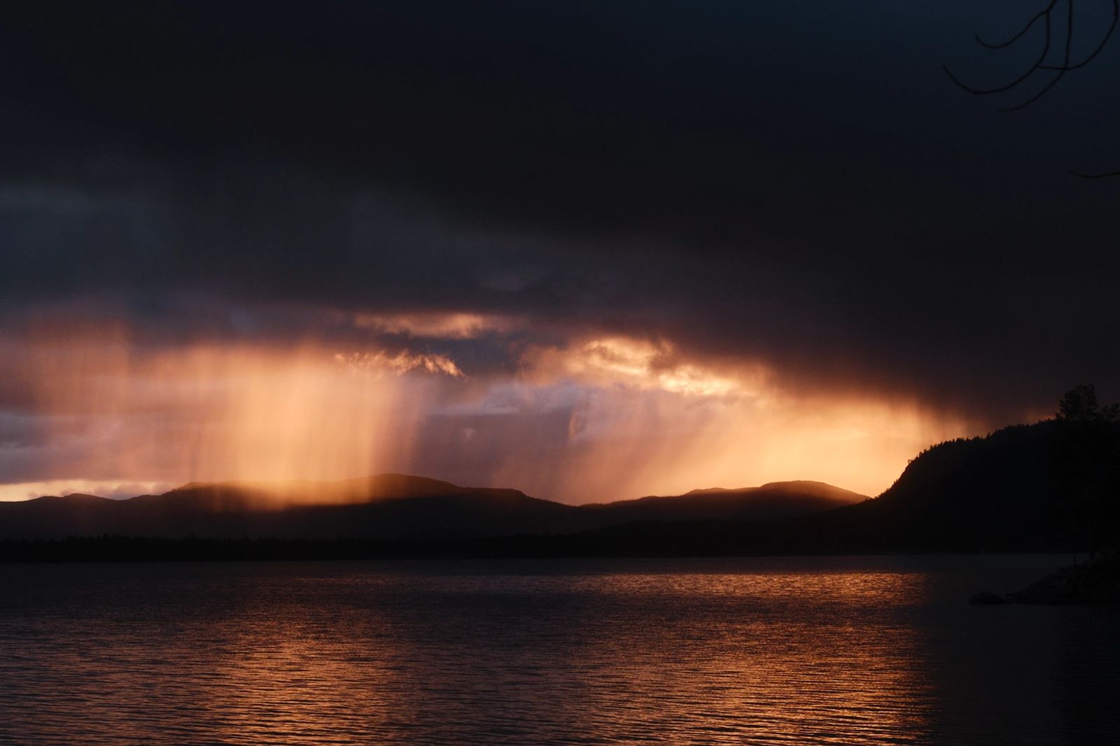 Dramatische Lichtstimmung über einem weiten See mit goldenen Sonnenstrahlen, die durch dunkle Regenwolken brechen.