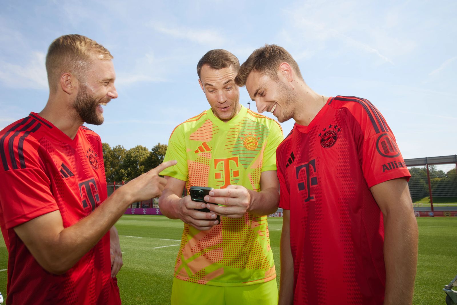Manuel Neuer, Konrad Laimer und Josip Stanišić blicken lachend auf ein Smartphone an der Säbener Straße